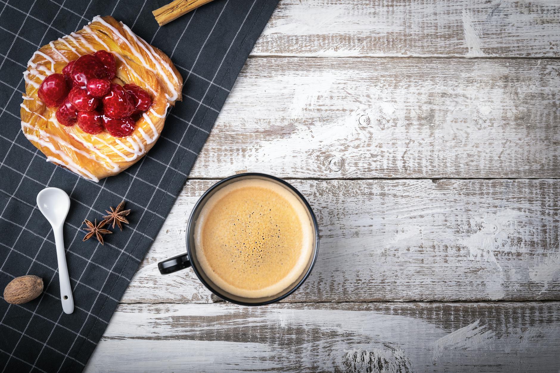 A delicious setup with coffee and raspberry pastry on a white wooden table